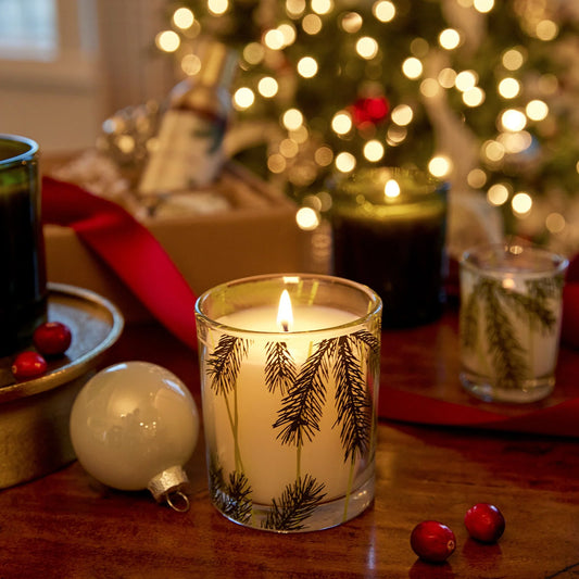 Candle by Lafco with pine tree design on a table with Christmas decorations