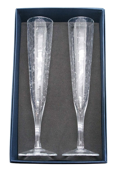 Two champagne flutes laying in navy blue Mariposa gift box.