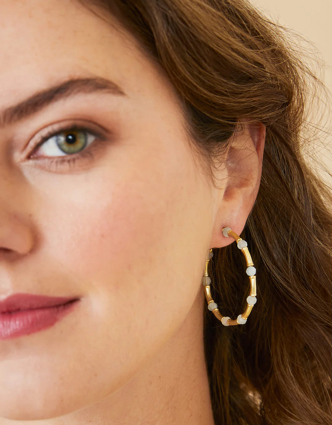 Close-up of a woman wearing a gold hoop earring with small beads.