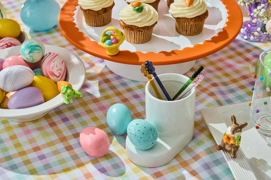Easter-themed table setting with cupcakes, candy, and decorative items on a checkered tablecloth.