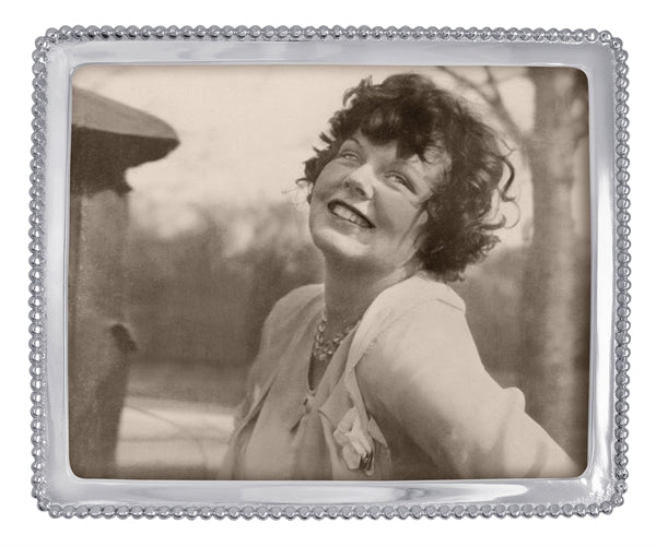 A silver frame with a thin frame and small silver beading around the edge. A  black and white stock photo of a woman with short hair smiling sits within the frame.