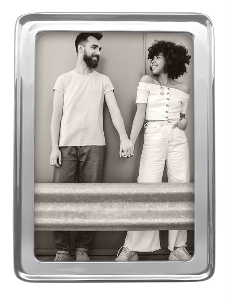 A silver 5" by 7" frame with a stock photo of a modern day couple holding hands by a guard rail.