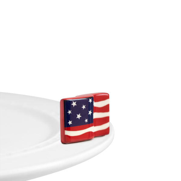 A porcelain waving American flag ornament a top a Nora Fleming dish.