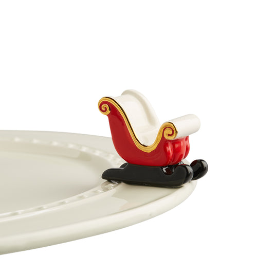 A miniature red and white sleigh ornament with a reindeer design, placed on a white plate with a white border.