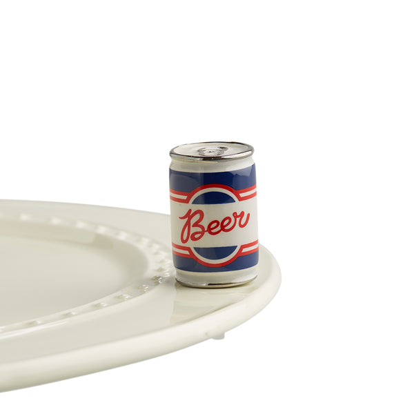 A porcelain red, blue and white beer can with beer written in center on top of Nora Fleming dish. 