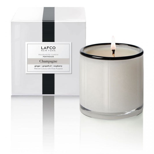 A beige candle with a clear lid, labeled 'Champagne' by Lafco, placed next to its white and black packaging box.